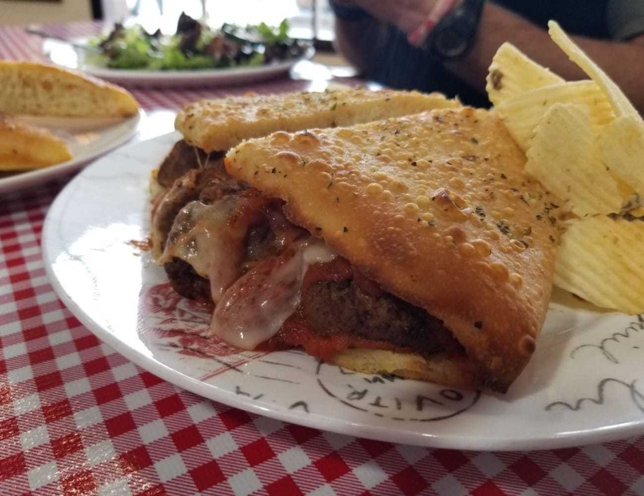 Pizza burger with melted cheese, served with potato chips on a checkered tablecloth.