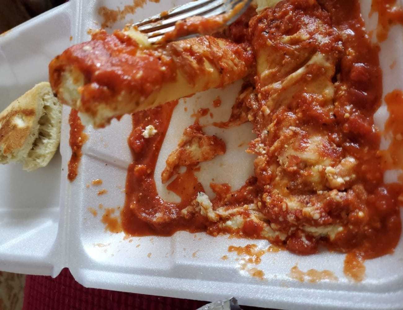 Cannelloni in tomato sauce on a takeout tray with a piece of bread.