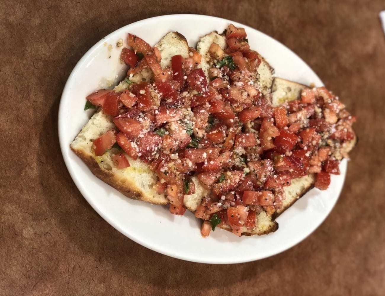 Bruschetta topped with diced tomatoes and herbs on an oval white plate.