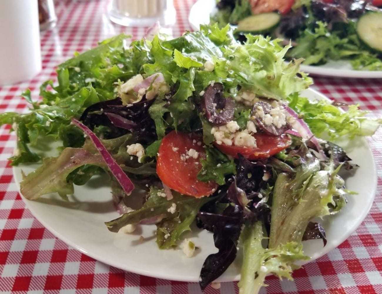 Mixed green salad with tomatoes, olives, and feta on a checkered tablecloth.
