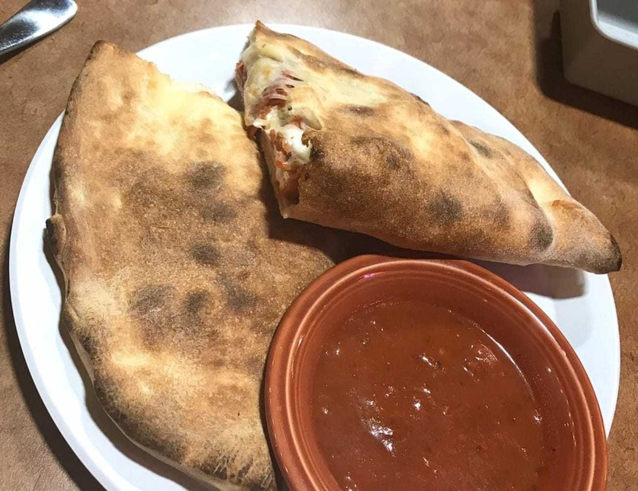 Calzone with marinara sauce on a white plate.