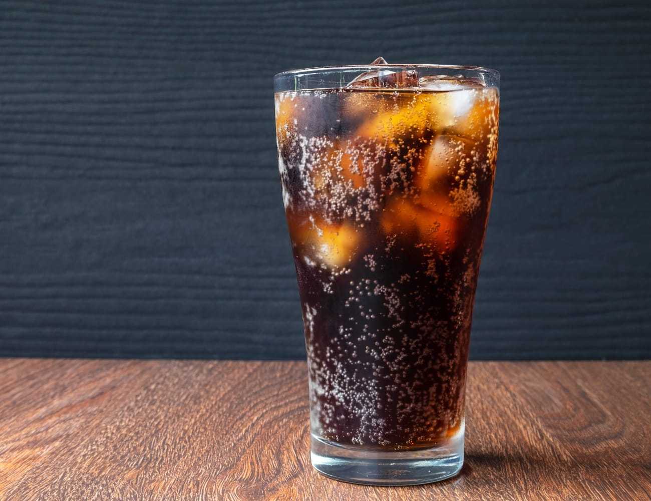 Chilled glass of cola with ice on a wooden table against a dark background.