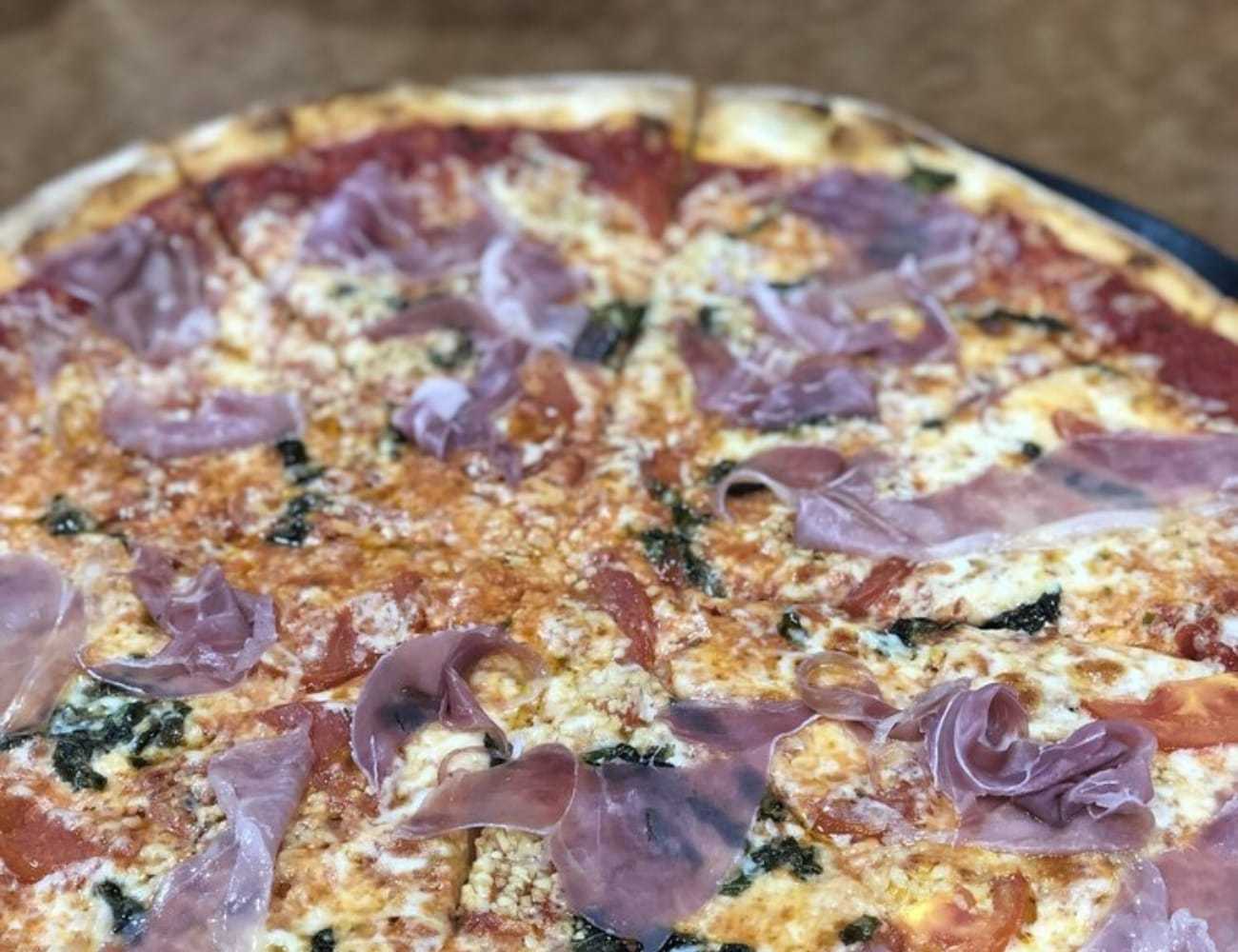 A pizza topped with prosciutto and cheese on a wooden table.