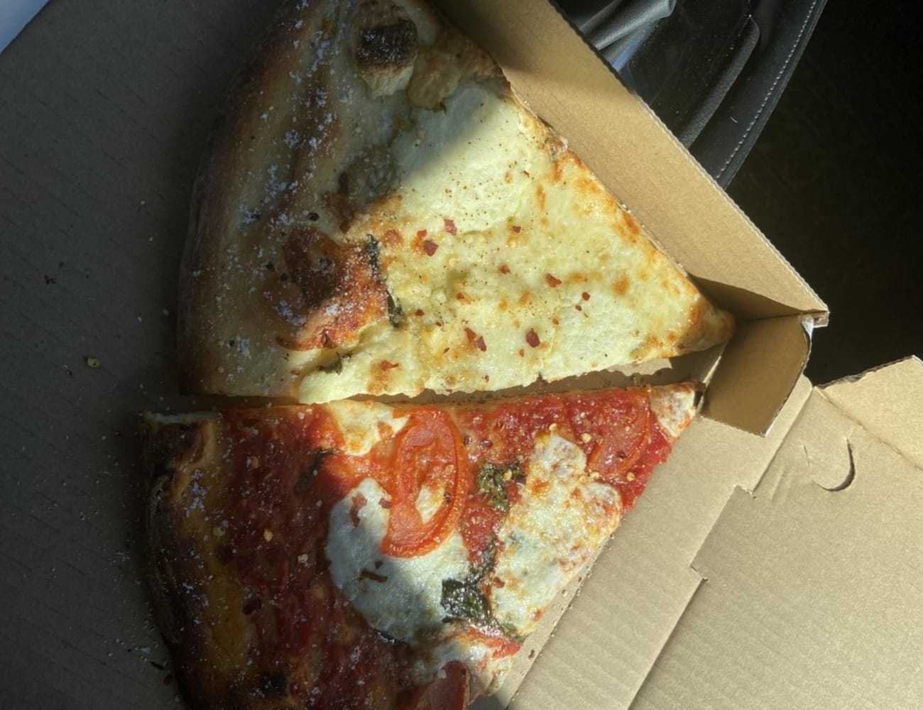 Two slices of pizza in a box, one with cheese and one with tomato and basil.